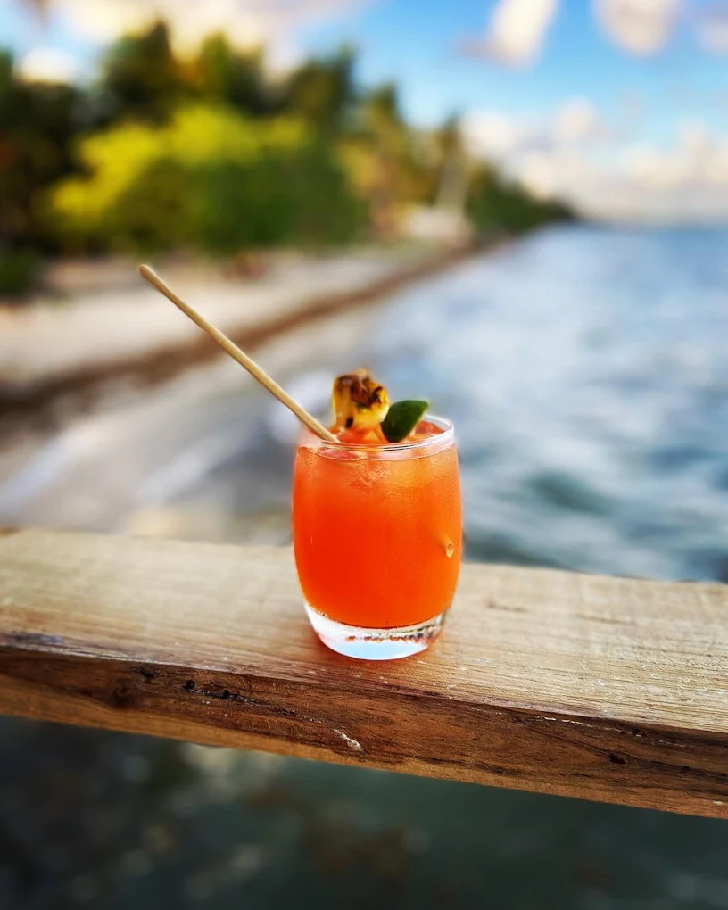 Orange tropical cocktail on a wooden rail beside the Caribbean